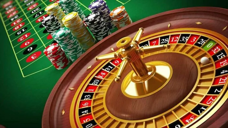 Vista en diagonal de un cilindro de ruleta con fichas apiladas al costado y el paño verde de apuestas al fondo.